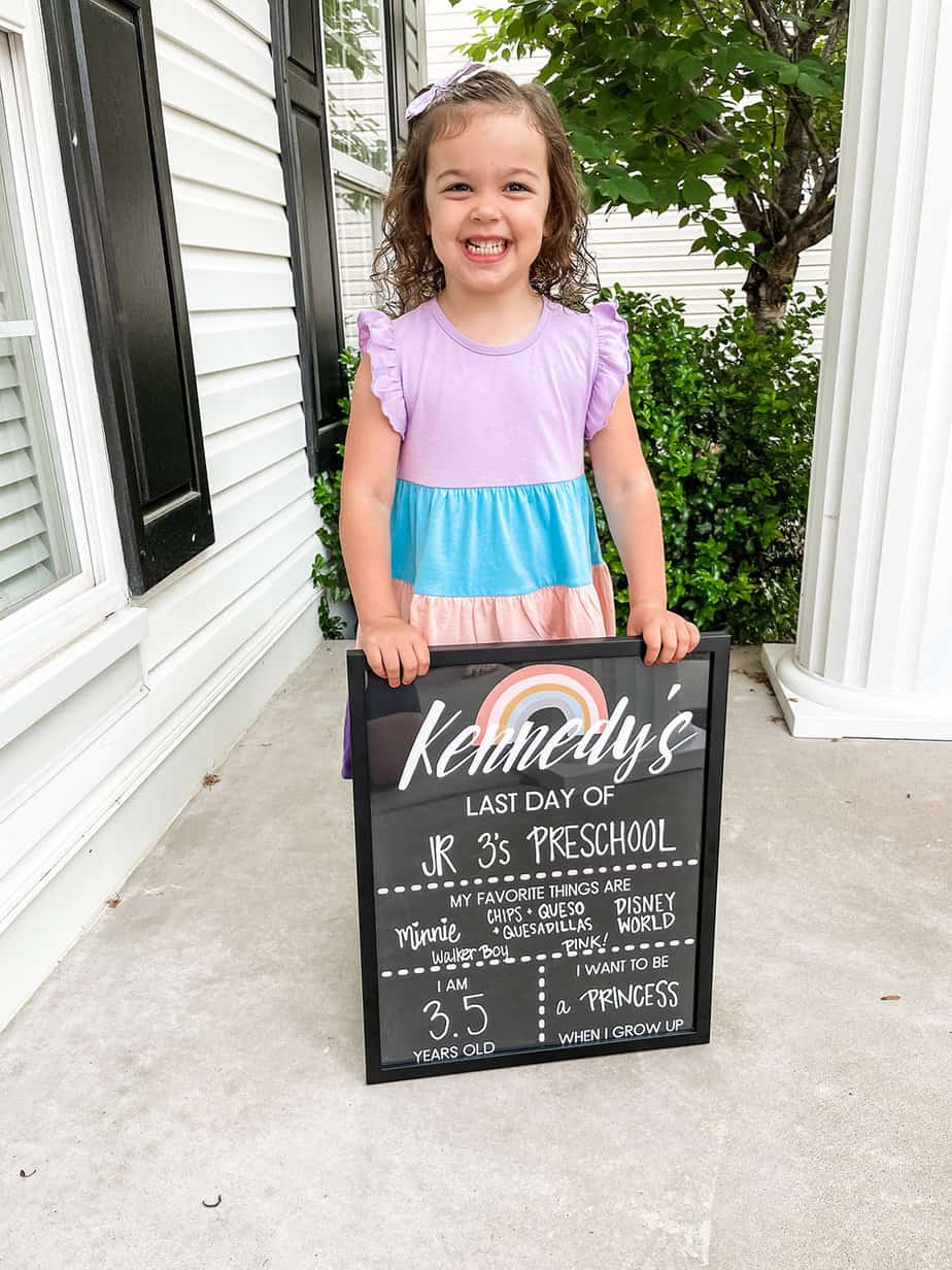 little girl in blue dress holding last day of school sign up on last day of preschool