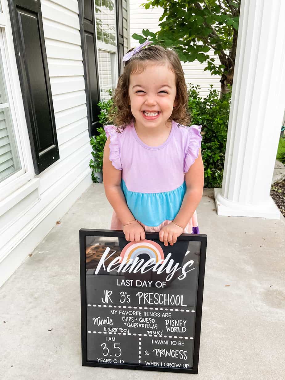 little girl in blue dress holding last day of school sign up on last day of preschool