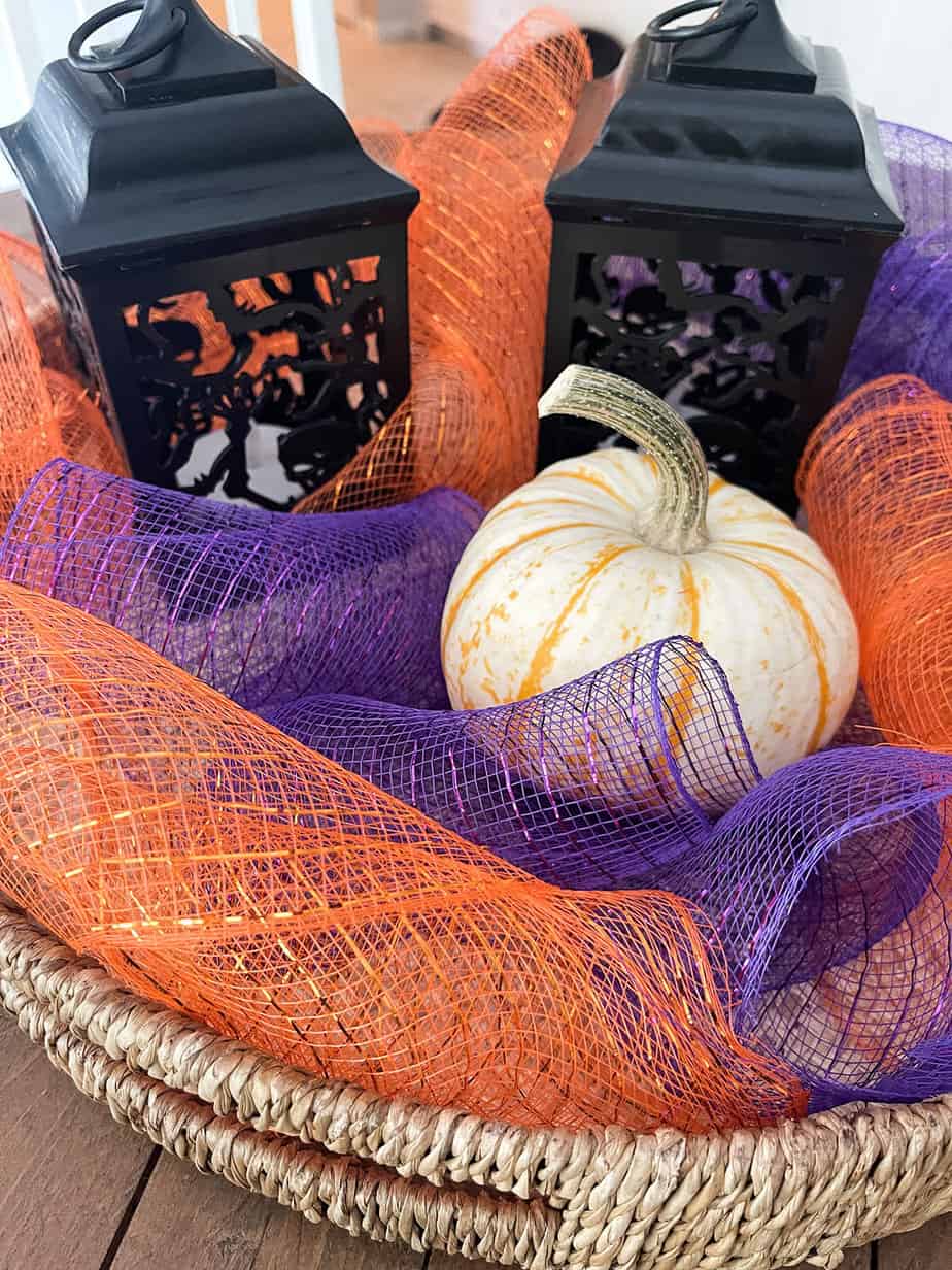Halloween centerpiece made with purple and orange mesh, small pumpkin and black halloween lanterns.