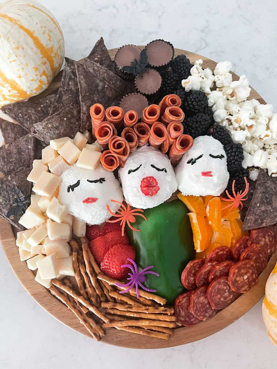 Hocus Pocus inspired charcuterie board made of cheese, meat, three cheese wheels as heads, fruit and veggies to look like Sanderson Sisters.