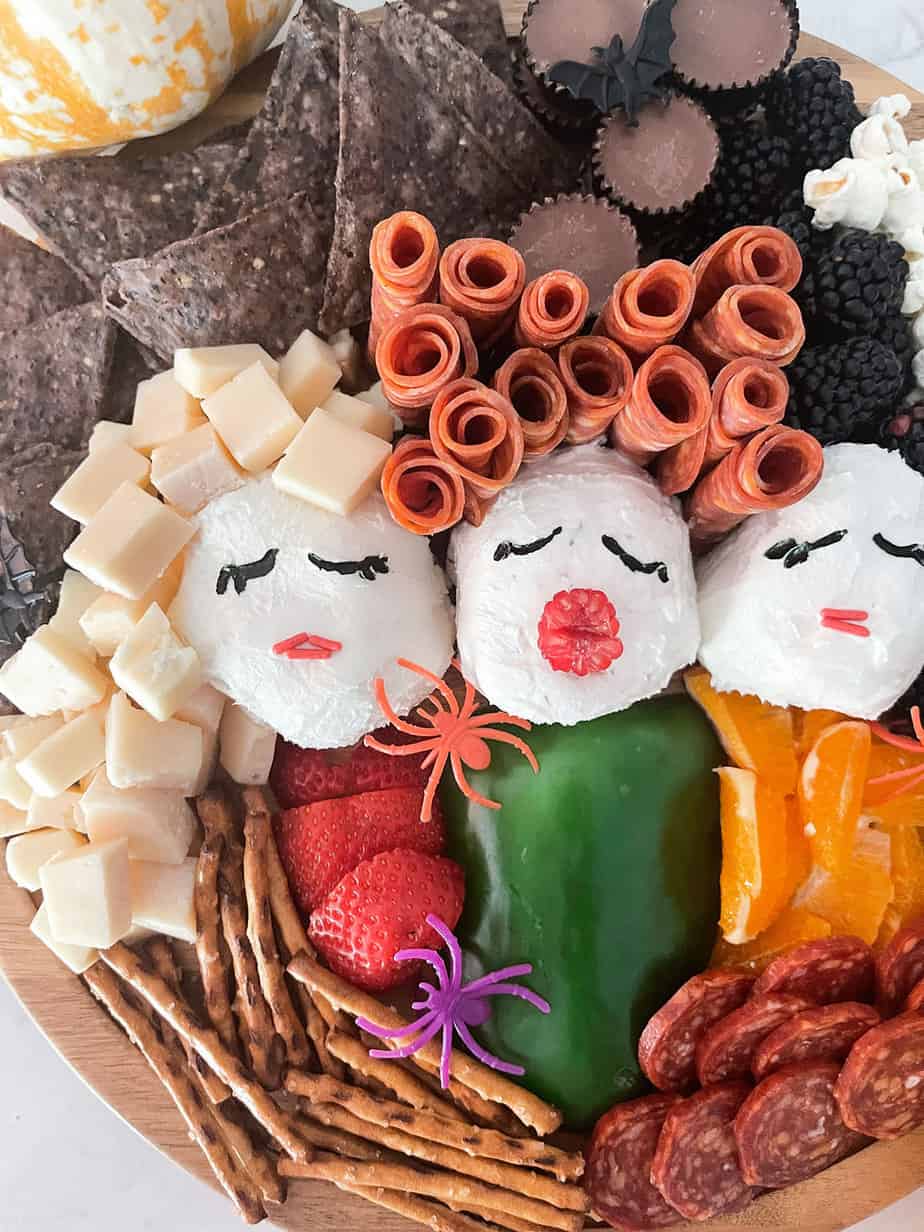 Hocus Pocus inspired charcuterie board made of cheese, meat, three cheese wheels as heads, fruit and veggies to look like Sanderson Sisters.