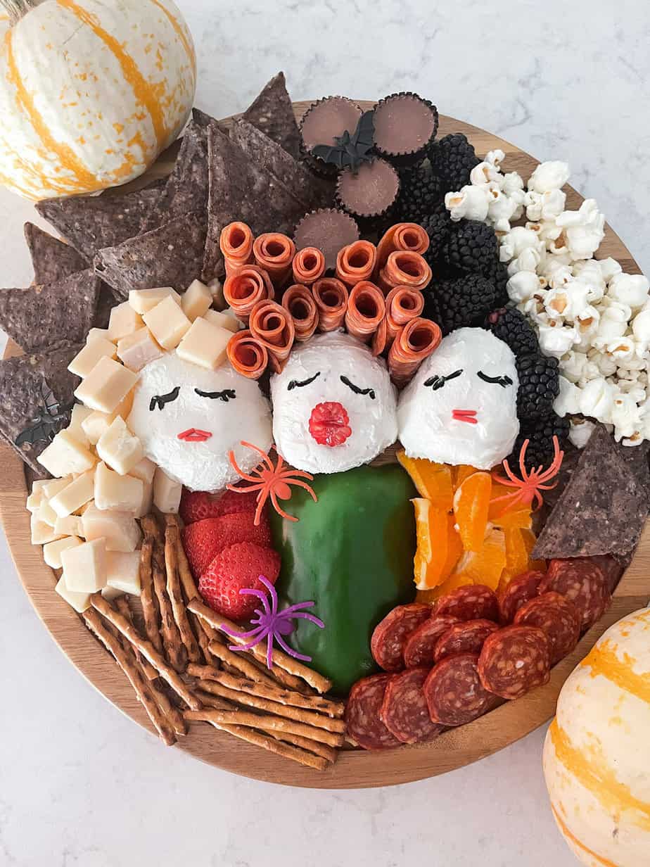 Hocus Pocus inspired charcuterie board made of cheese, meat, three cheese wheels as heads, fruit and veggies to look like Sanderson Sisters.