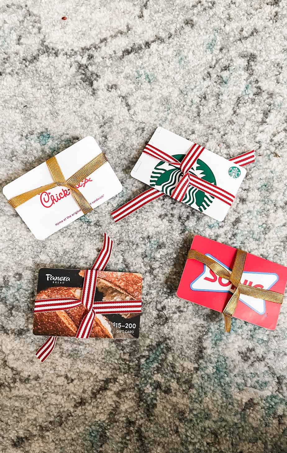 gift cards to chick-fil-a, starbucks, sonic, and panera with ribbon wrapped around them to look like presents laying on a cream and blue rug