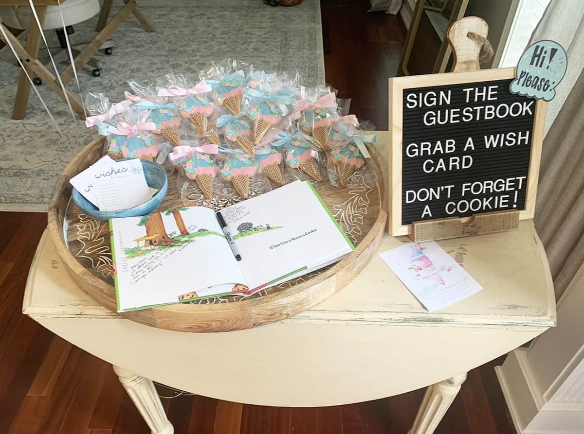 Table at baby shower with ice cream shaped cookies as favors and a children's book for people to sign and use as a guestbook.