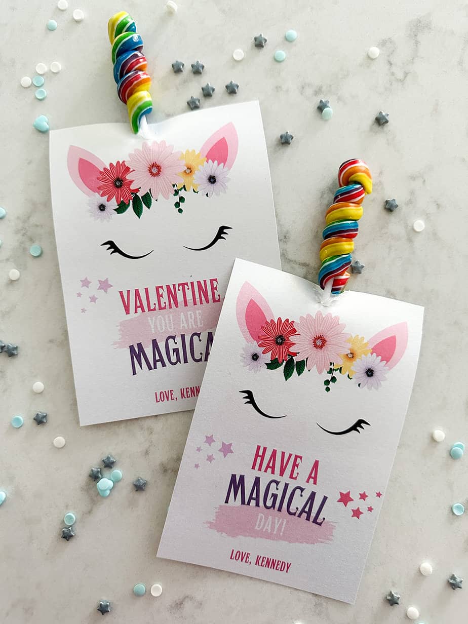 Unicorn valentine cards with a twisty colorful lollipop used as the unicorn's horn laying on a white countertop.