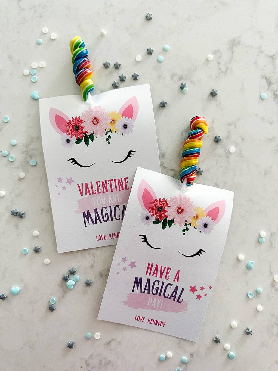 Unicorn valentine cards with a twisty colorful lollipop used as the unicorn's horn laying on a white countertop.