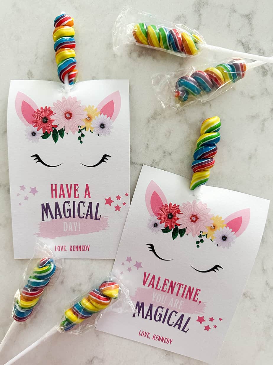 Unicorn valentine cards with a twisty colorful lollipop used as the unicorn's horn laying on a white countertop.