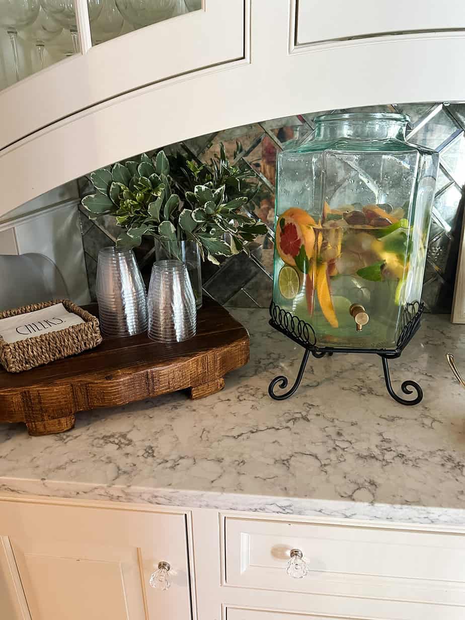 glass dispenser filled with fresh citrus and mint leaves to make pretty water for a baby shower, sitting next to fresh flowers and plastic cups.