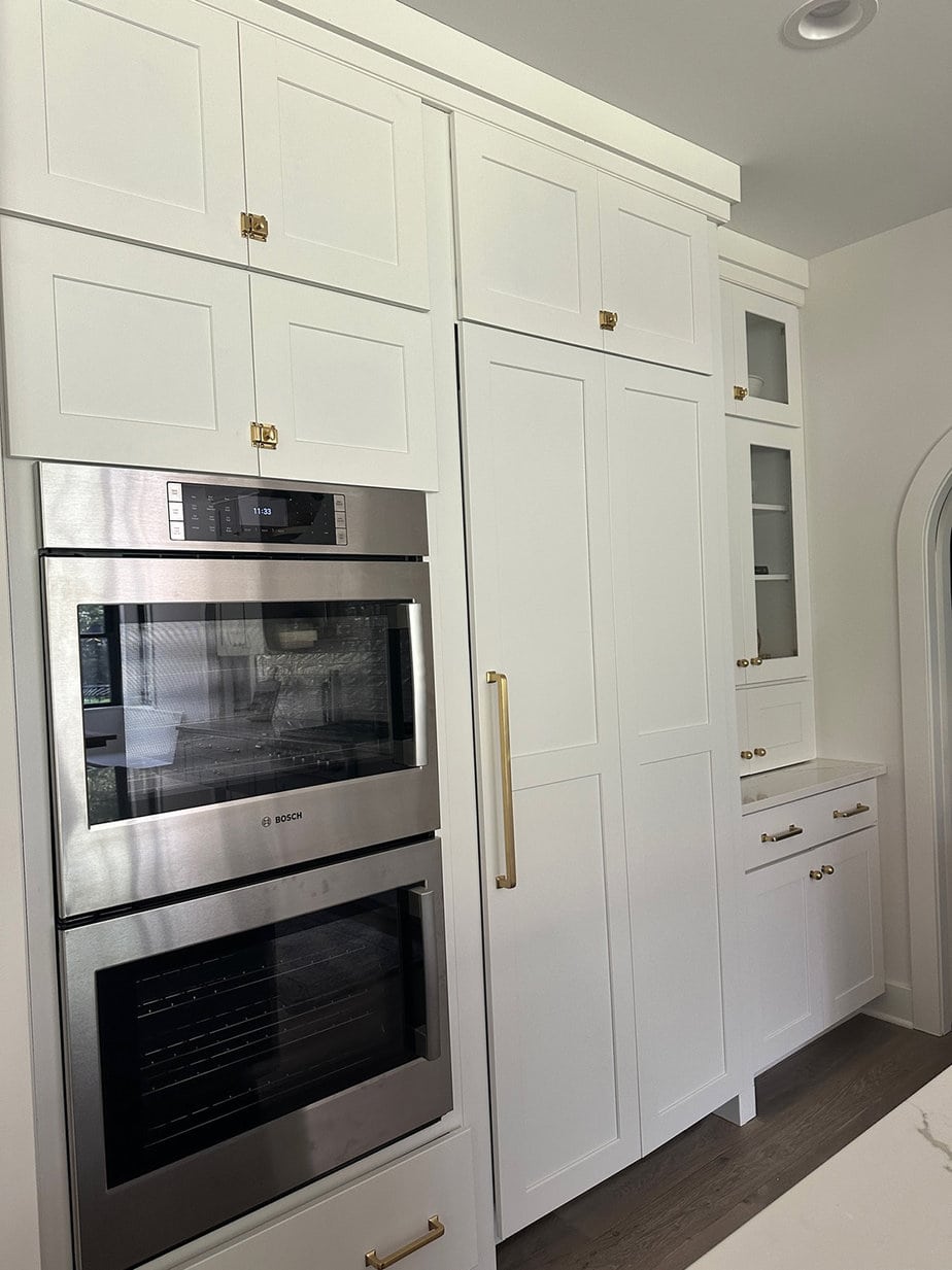 White kitchen cabinets with a panel fridge built in and aged brass hardware throughout