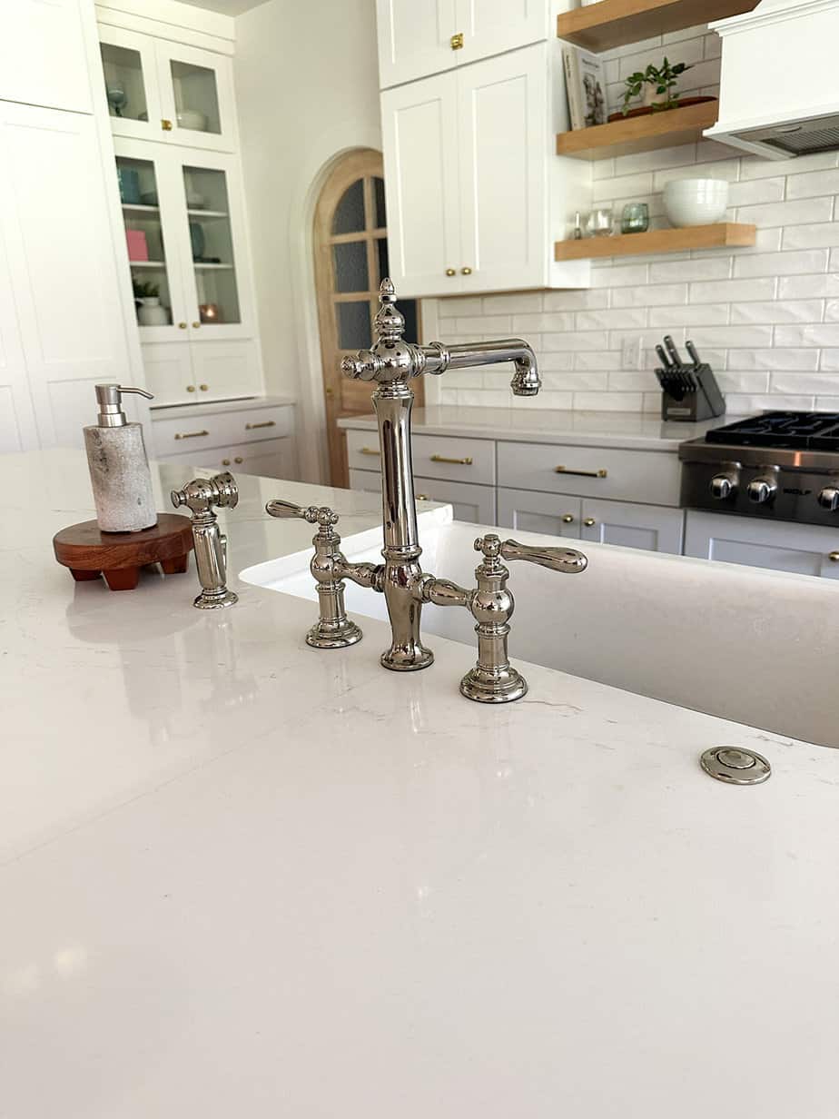 polished nickel bridge faucet sitting in a blue kitchen island with thick white quartz countertops