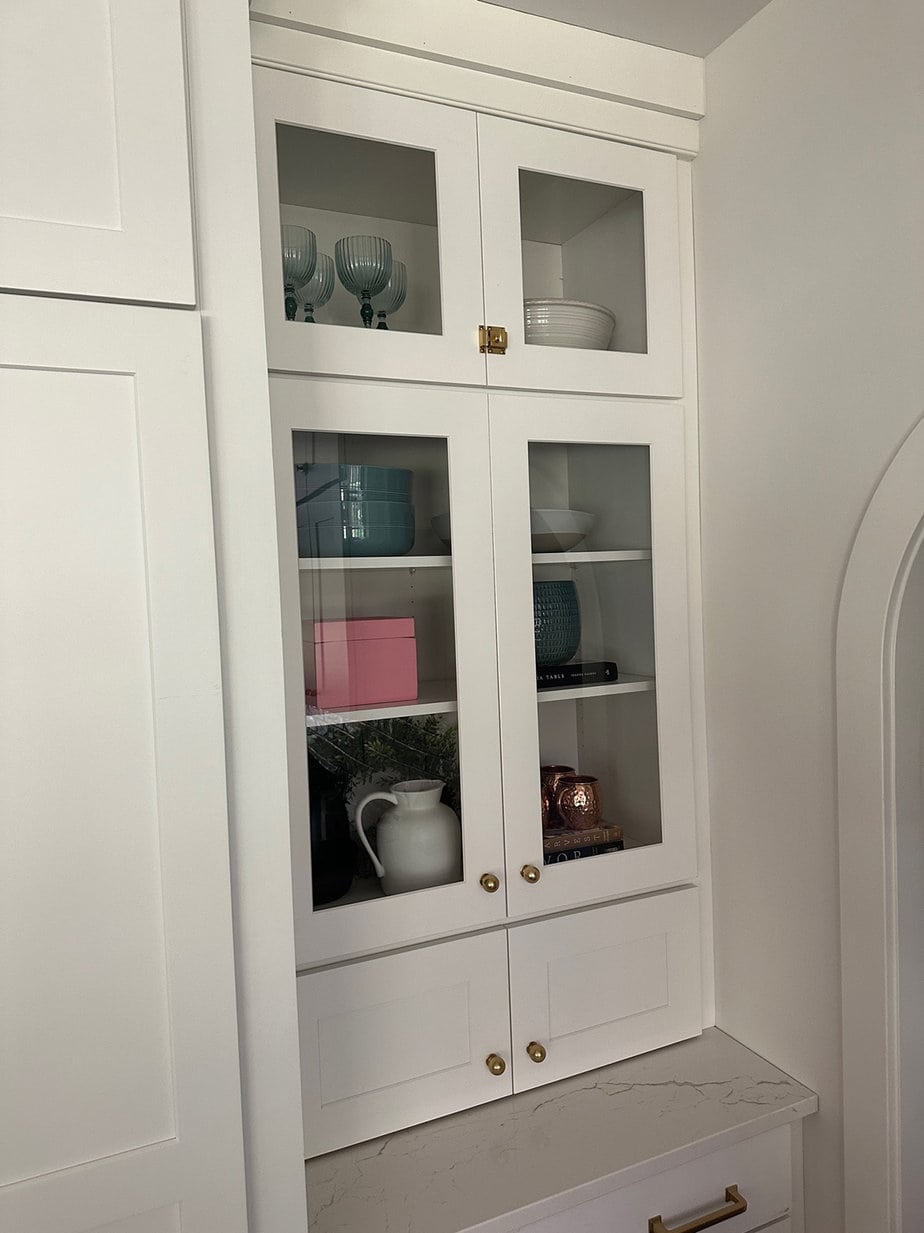 White kitchen cabinets with a glass fronts, a hidden appliance garage, and aged brass hardware throughout