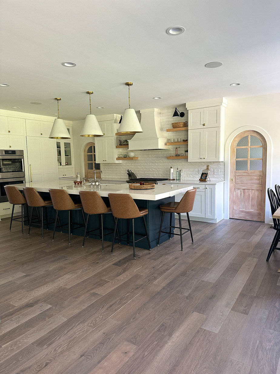 transitional style white kitchen with blue island, arched pocket doors on either side of range wall that has white backsplash. mixed metals of polished nickel, aged brass, and matte black.