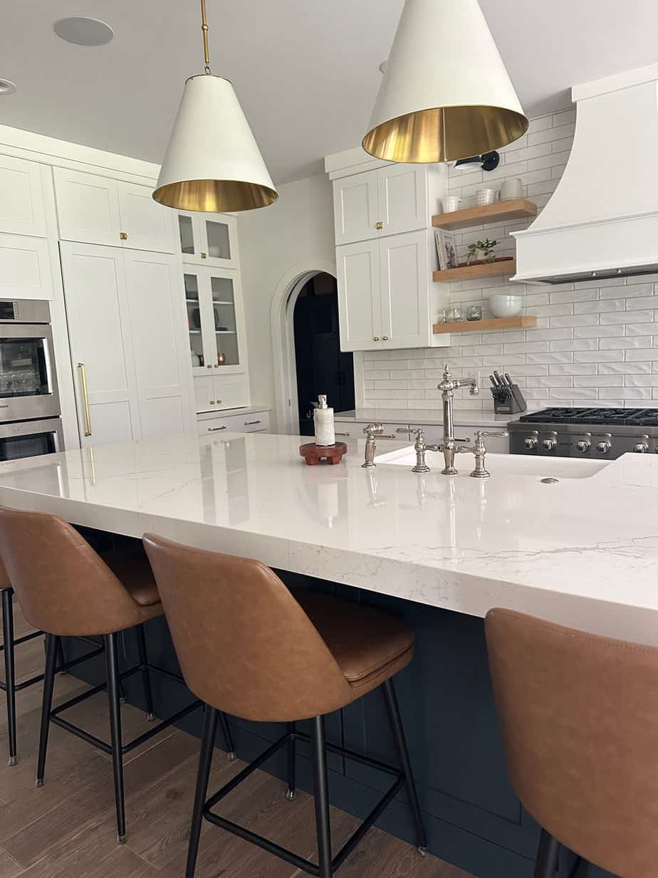 white transitional kitchen with white and brass metal pendants over a blue island with white quartz countertops