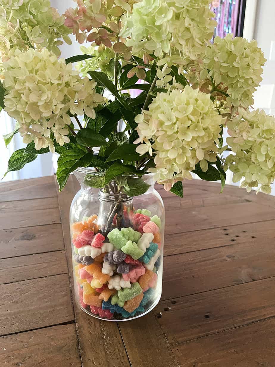 flower vase filled with brightly colored candy and large white hydrangeas used as a centerpiece for ice cream themed party