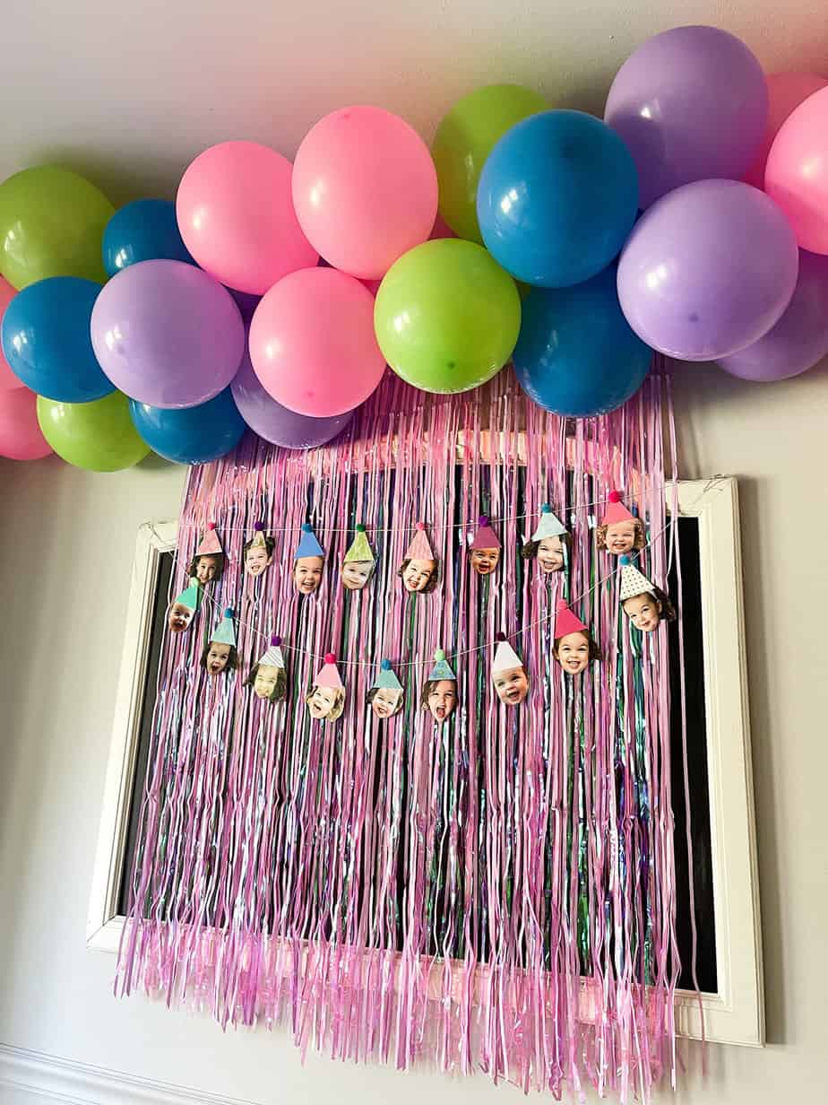 diy balloon garland with hot pink, purple, bright blue, and lime green balloons on top of a hot pink fringe photo back drop