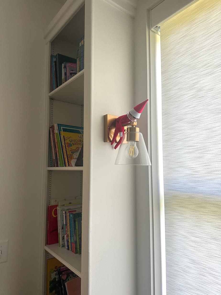 elf on the shelf hanging off of a light fixture in kids playroom