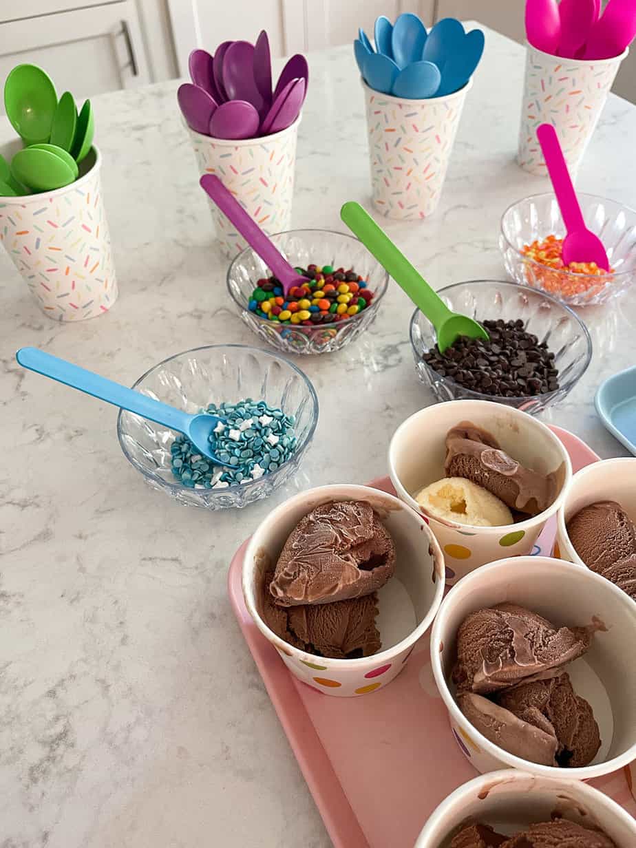 ice cream bar for party set up with colorful spoons, bowls of toppings, and prescooped ice cream bowls