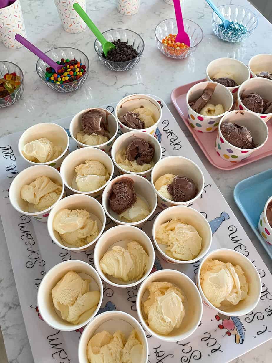 ice cream bar for party set up with colorful spoons, bowls of toppings, and prescooped ice cream bowls