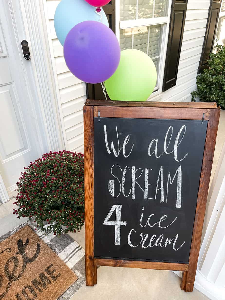 ice cream chalkboard art at front door welcoming guests to party with bright colored balloons tied to the back