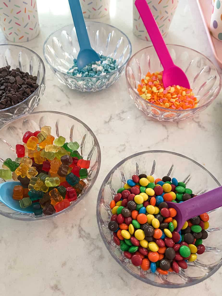 ice cream bar for party set up with colorful spoons, bowls of toppings, and prescooped ice cream bowls