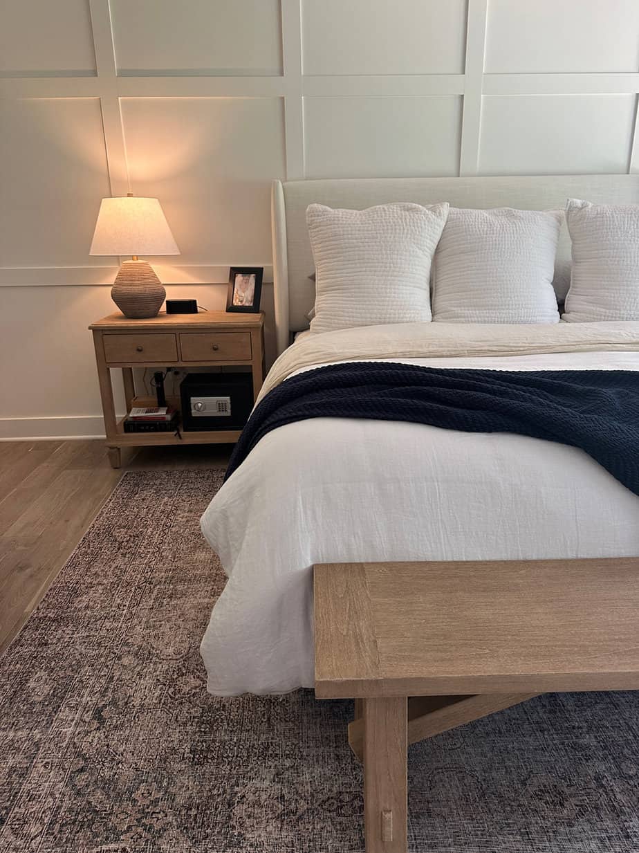 neutral master bedroom with accent wall, white bedding, natural wood details and roman shades