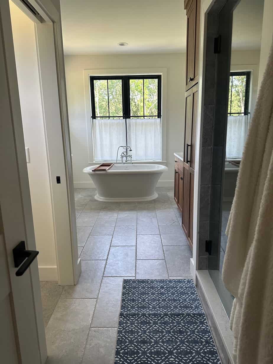 master bathroom freestanding white tub with chrome fixture, black windows, cafe curtains and gray tile