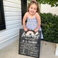 little girl in blue dress holding first day of school sign up on first day of preschool